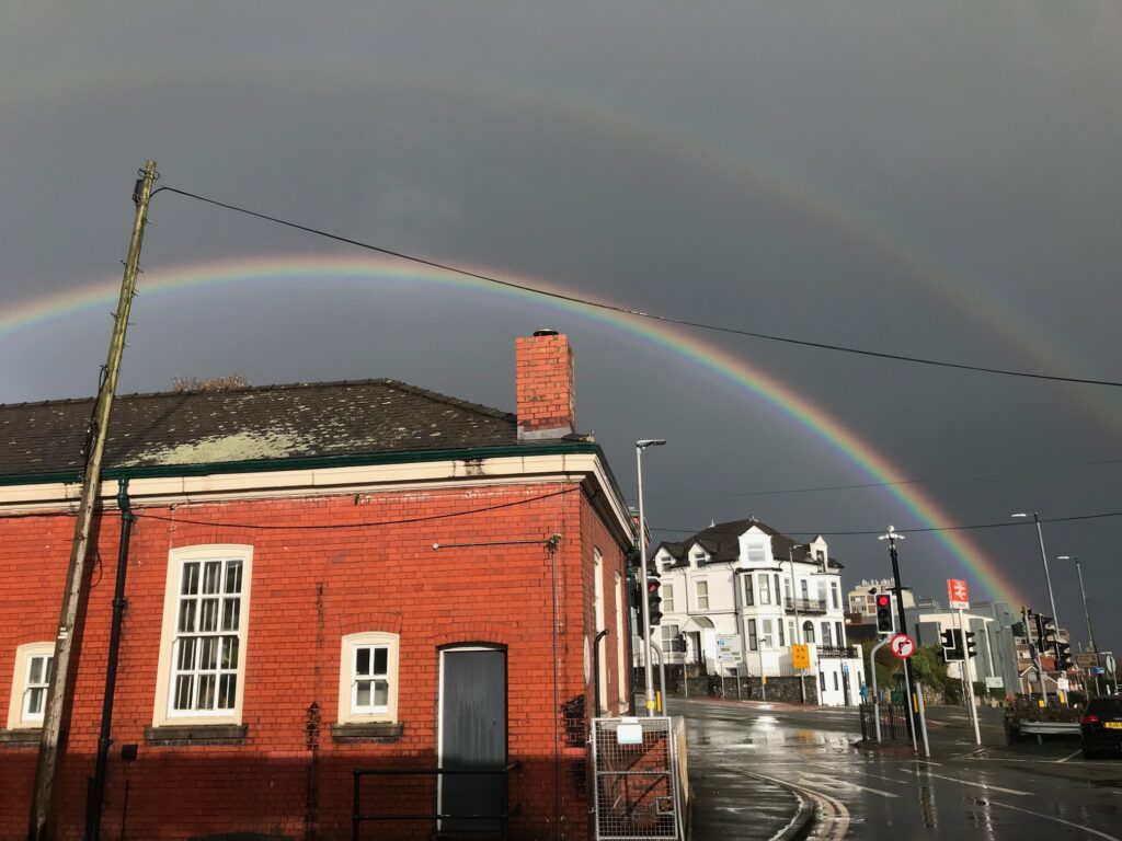 Two rainbows, one distinct, one faint, against a dark cloudy sky with a red brick building in the front.